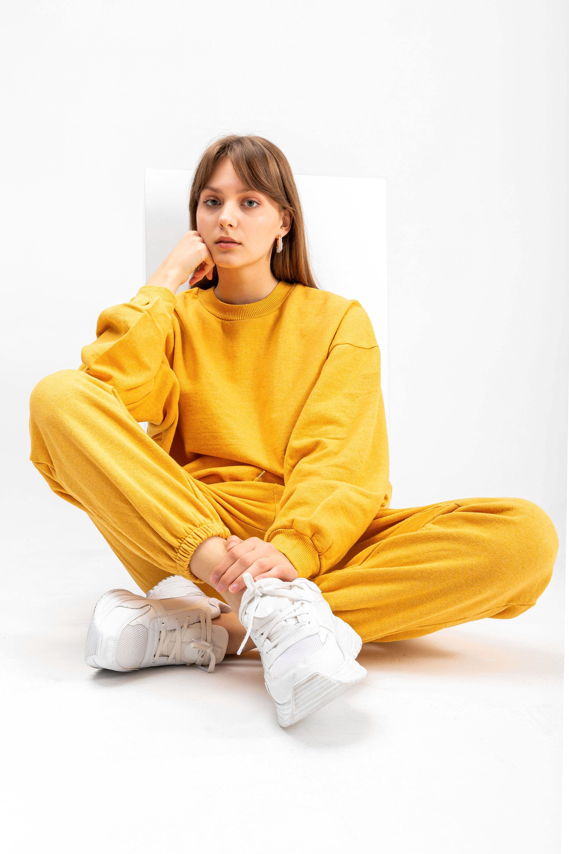 Young girl in yellow tracksuit and sports shoe lying on cube  isolated on white